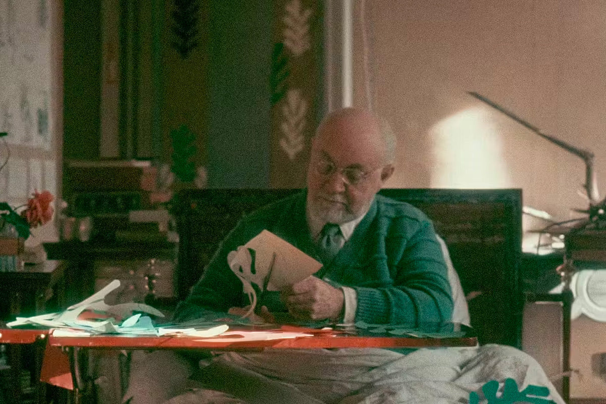 Henri Matisse à la fin de sa vie, découpant des formes dans du papier peint à la gouache, assis à sa table